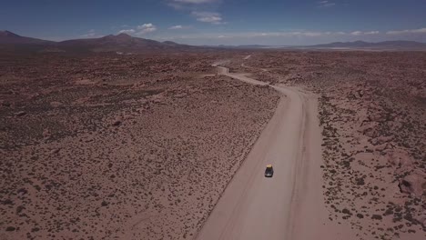 Aerial-view-of-a-4x4-on-a-dusty-red-road-at-the-Eduardo-Avaroa-National-Andean-Wildlife-Reserve,-slowly-lifting-the-view-to-open-up-to-the-valley-of-rocks,-"Valle-de-Rocas"-in-Uyuni,-Bolivia