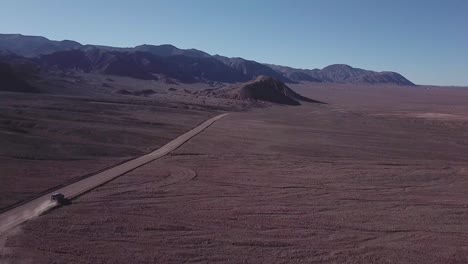 Auto-Fährt-Auf-Einer-Staubigen-Straße-In-Der-Atacama-Wüste-Mit-Einer-Trockenen-Landschaft-Im-Norden-Chiles_Follow-Shot