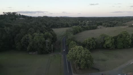 Green-flat-light-aerial-follows-vehicle-on-suburb-estate-road-in-NSW