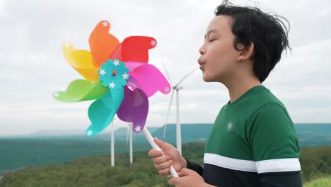 Fortschrittlicher-Junger-Asiatischer-Junge,-Der-Mit-Windturbinenspielzeug-Im-Windturbinenpark-Spielt.