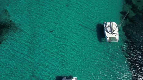 Catamaran-Sailboats-anchored-in-clear-blue-lagoon-on-sunny-day,-Sardinia