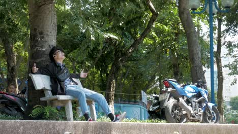 Ein-Bewohner-Von-Hanoi-Genießt-Es,-Auf-Einer-Parkbank-Platz-Zu-Nehmen-Und-Musik-Zu-Hören