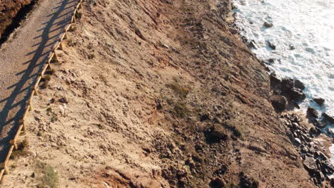 Revealing-aerial-of-Portugal-coastal-area,-hiking-pathway-goes-along-the-coast-with-cliffs-rising-straight-up-from-the-beach,-scenic-headland-coast-of-Portugal,-traveling-and-vacation-concept