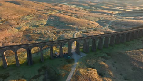 Arched-railway-bridge-viaduct-spanning-bare-moorland-with-dirt-track-at-sunrise-in-winter