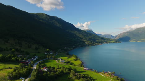Vibrant-rolling-green-forested-hills-in-shadow-of-fjord,-stunning-turquoise-water-shines-in-the-sun