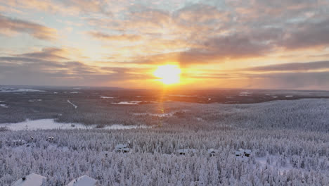Aerial-view-a-arctic-sunset-behind-mountain-huts-and-and-frozen-forest-of-Lapland