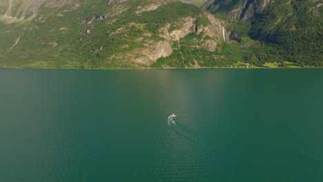 El-Seguimiento-Con-Drones-Sigue-A-Una-Embarcación-Que-Acelera-Y-Gira-En-Las-Aguas-Verdes-Del-Fiordo-De-Lustra,-Noruega