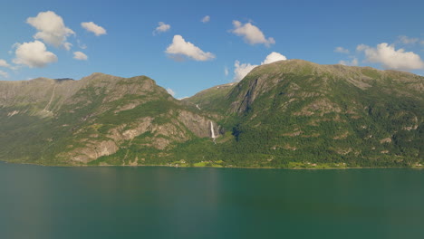 Aerial-establishing-overview-of-waterfall-cascading-in-distance-of-Lustra-Fjorden-Fjord-Norway-in-the-summer