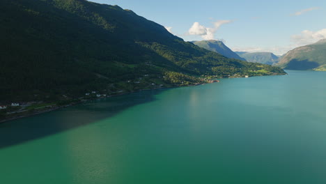 Panoramic-aerial-overview-of-quaint-town-in-shadow-of-stunning-fjord-in-Lustra-Fjorden,-Norway