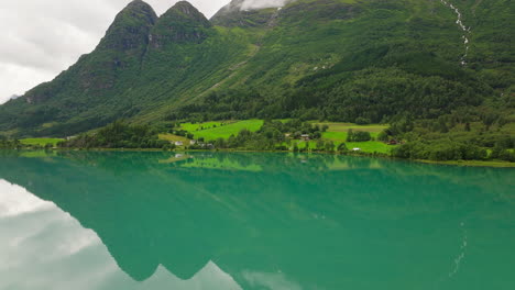 Aerial-parallax-around-Oldevatnet-glacial-lake-water-reflecting-forested-mountain-above,-Norway