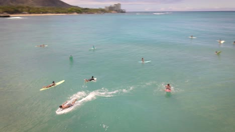 Aerial-footage-of-surfers-catching-a-wave-in-the-middle-of-the-ocean-with-perfect-weather-and-clean-water-in-Hawaii-paradise,-shot-on-drone-from-above