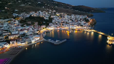 Aerial-drone-view-of-village-of-Batsi-with-traditional-taverns-and-clear-water-beach,-Andros-island,-Cyclades,-Greece,-at-dusk