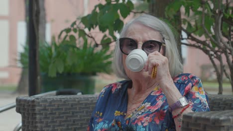 Lovely-older-woman-with-sunglasses-sips-her-tea-with-a-cookie-in-her-hand-on-a-sunny-day