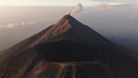 Aerial-tilt-shot-in-front-of-a-huge-crater-with-smoking-Fuego-volcano-background