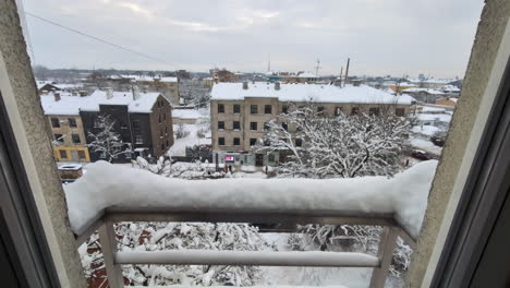 Snow-piles-up-on-balcony-railing,-slow-motion-push-in-to-old-neighborhood-industrial-buildings-in-white