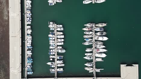 Drone-top-down-bird's-eye-view-of-boats-docked-in-modern-concrete-port,-sailboat-textured-pattern