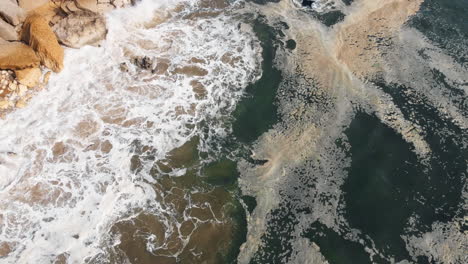 Aerial-view-of-rocky-beach-with-crashing-waves-in-Nazare,-Portugal