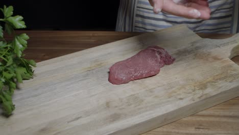 Chef-adds-salt-with-hands-to-flavor-beef-steak-on-kitchen-wooden-board