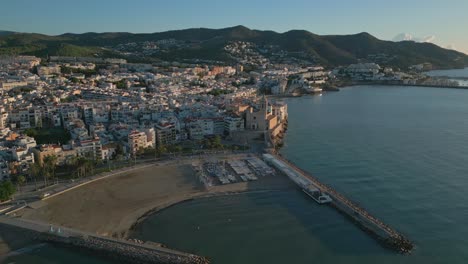 Aerial-view-over-Sitges-sunrise,-Barcelona-southwest,-Yacht-club-and-church
