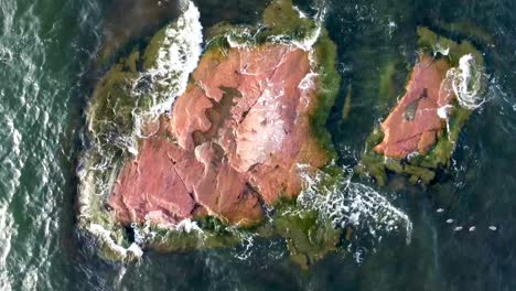 Eine-Umgekehrte-Luftaufnahme-Einer-Kleinen-Felseninsel-Im-See-Mit-Wellenflut