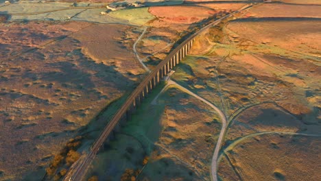 Long-railway-bridge-with-arches-spanning-desolate-winter-moorland-with-dirt-road-crossing-frame