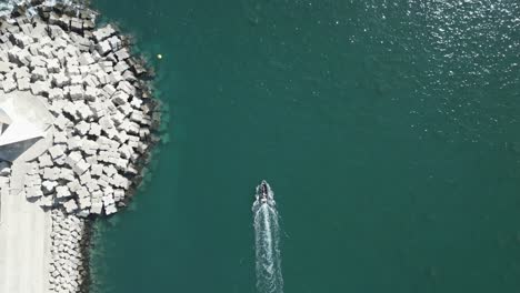 Drone-top-down-tracking-follows-boat-with-large-wake-exiting-from-harbor-around-breakwater-jetty