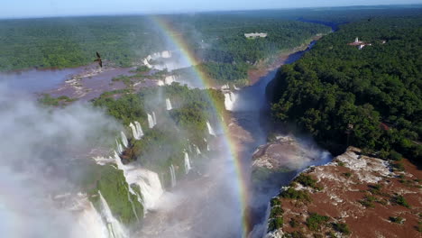 A-breathtaking-bird's-eye-view-of-Iguazu-Falls,-adorned-with-numerous-birds-and-a-stunning-rainbow