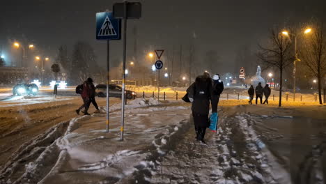 Pendler-Laufen-Abends-über-Schneebedeckte-Gehwege,-Während-Straßenlaternen-Den-Weg-Beleuchten