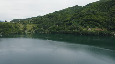 Antena-Siguiendo-Un-Barco-En-El-Lago-Plivsko-En-Jajce,-Panorama-De-La-Naturaleza-Balcánica,-Nublado