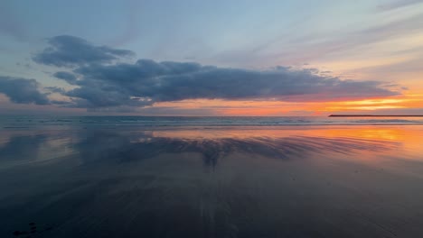 Time-lapse-of-clouds-moving-towards-a-tranquil-beach-with-a-spectacular-sunset-over-the-horizon