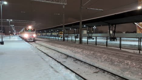 Commuter-train-enters-station-in-slow-motion,-covered-in-snow-on-cold-winter-night