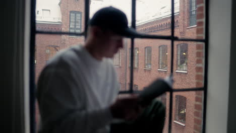 Focused-individual-reading-by-a-frosty-window,-with-a-historic-brick-building-backdrop-on-a-wintry-day