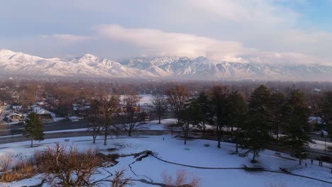 Seagulls-soar-above-snow-covered-icy-pond-in-park-with-epic-view-of-Wasatch-mountains-and-downtown-Salt-Lake-in-winter