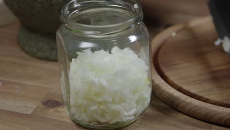 Adding-chopped-onion-to-a-glass-jar,-close-up