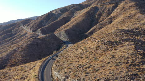 Drone-shot-of-cars-traveling-winding-mountain-road-cut-through-mountain-side