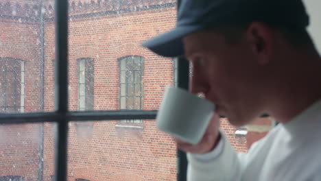 Young-man-enjoying-a-warm-drink-by-the-window-on-a-snowy-day