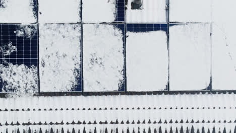 Aerial-top-down-shot-over-melting-solar-panels-on-a-snowy-house-roof,-winter-day