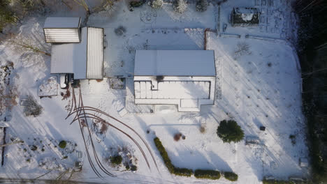 Birds-eye-drone-shot-above-a-snowy-house-with-solar-panels-on-the-roof,-winter-day