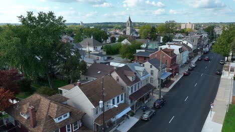 Aerial-rising-shot-of-a-town-street-lined-with-row-houses-and-a-church-spire-in-the-distance-in-USA