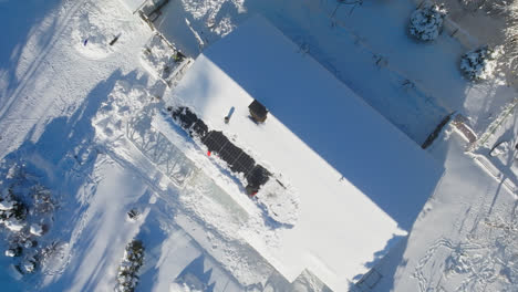 Luftaufnahme-über-Einem-Mann,-Der-Schnee-Von-Einem-Solarzellendach-Räumt,-Wintertag