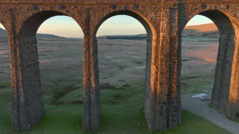 Railway-bridge-arch-fly-through-to-barren-winter-moorland-at-dawn