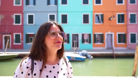 Woman-with-glasses-impressed-by-Burano-colorful-buildings-and-smiling-at-camera