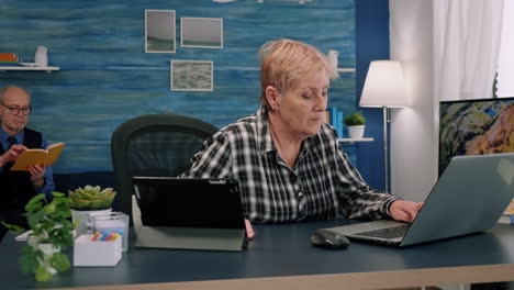 Old-manager-woman-typing-on-laptop-and-reading-on-tablet-in-same-time