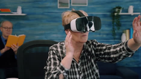 Retired-concentrated-senior-woman-using-virtual-reality-goggles-in-living-room