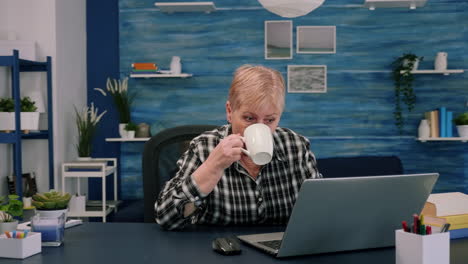 Ältere-Frau-Genießt-Eine-Tasse-Kaffee,-Während-Sie-Am-Laptop-Arbeitet