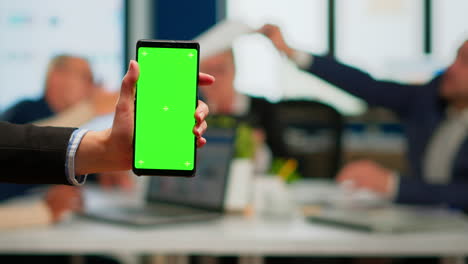 Businesswoman-holding-smartphone-with-green-screen-during-conference