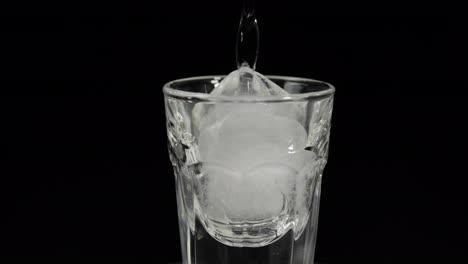 Pour-vodka-into-shot-glasses-with-ice-cubes-placed-on-a-black-background