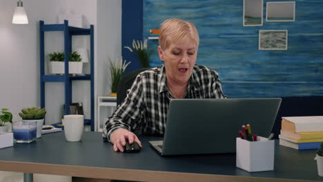 Old-middle-aged-businesswoman-working-at-laptop-typing-financial-data