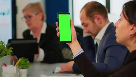 Businesspeople-analysing-reports-sitting-at-desk,-while-employee-holding-phone-with-green-screen