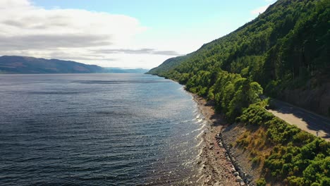 Aerial-View-Along-Loch-Ness-Coast-with-Lush-Green-Forest,-Scottish-Highlands,-Scotland